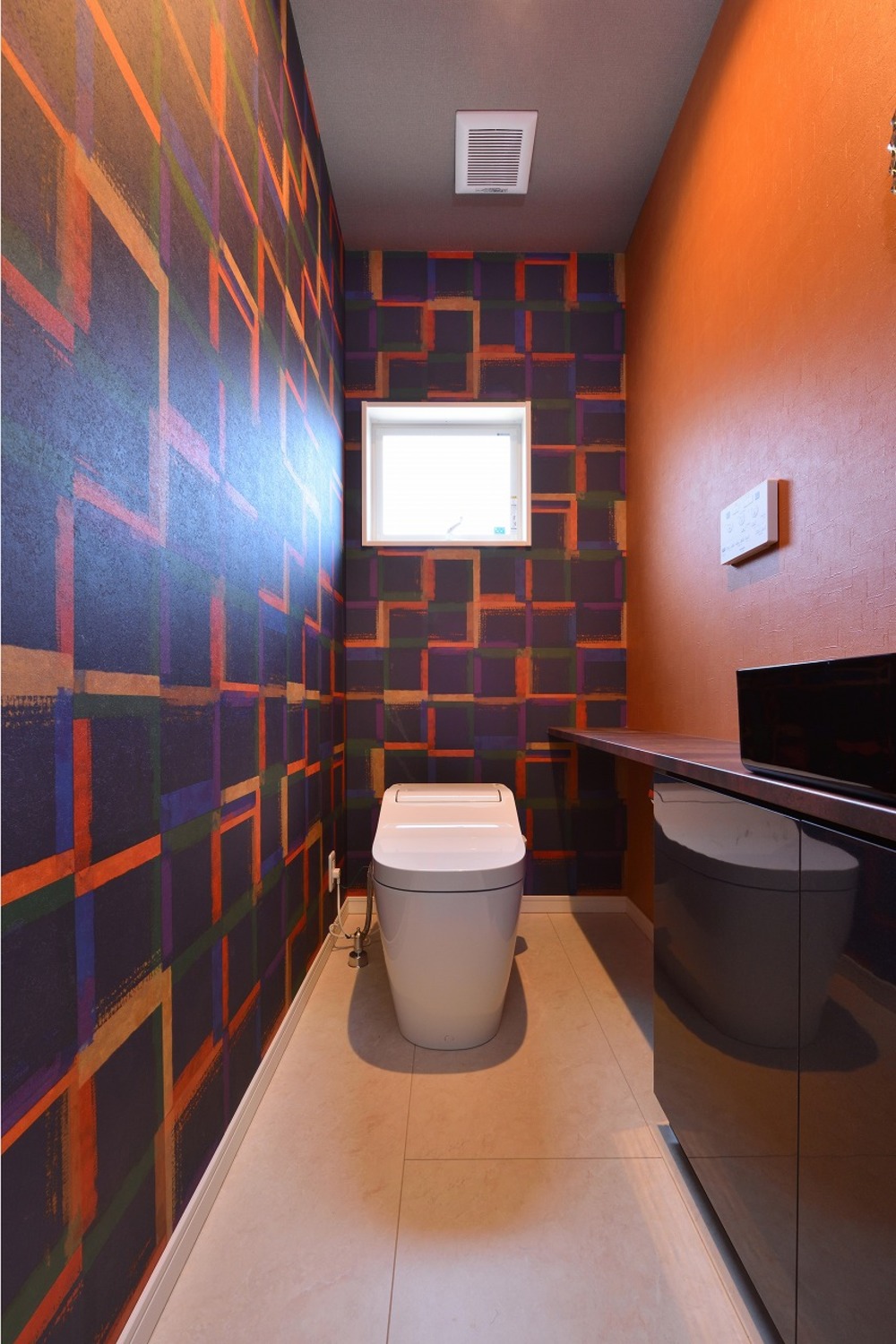 オレンジを基調とした幾何学模様のクロスが張られた２階トイレ